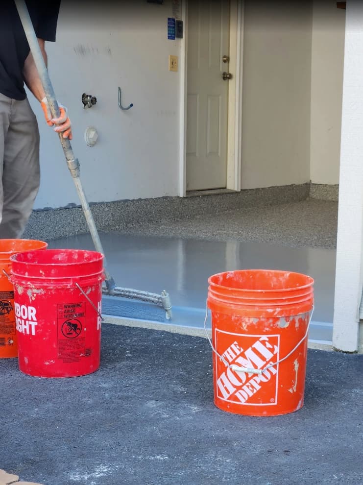 Installer spreading wet grey polyurea base coat across a prepped garage floor with a squeegee